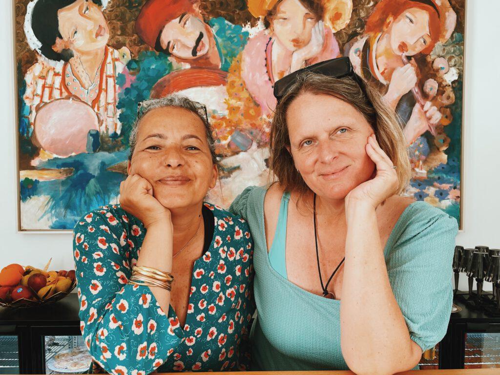 links: Myriam Maatoug, Besitzerin des Dar Oomi, Resort rechts: Andrea Philippi, Pressereferentin, Fremdenverkehrsamt Tunesien Porträt zweier Frauen vor einem Gemälde 